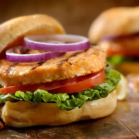 Hamburguesa de salmón jugosa y casera servida con lechuga fresca, tomate y cebolla